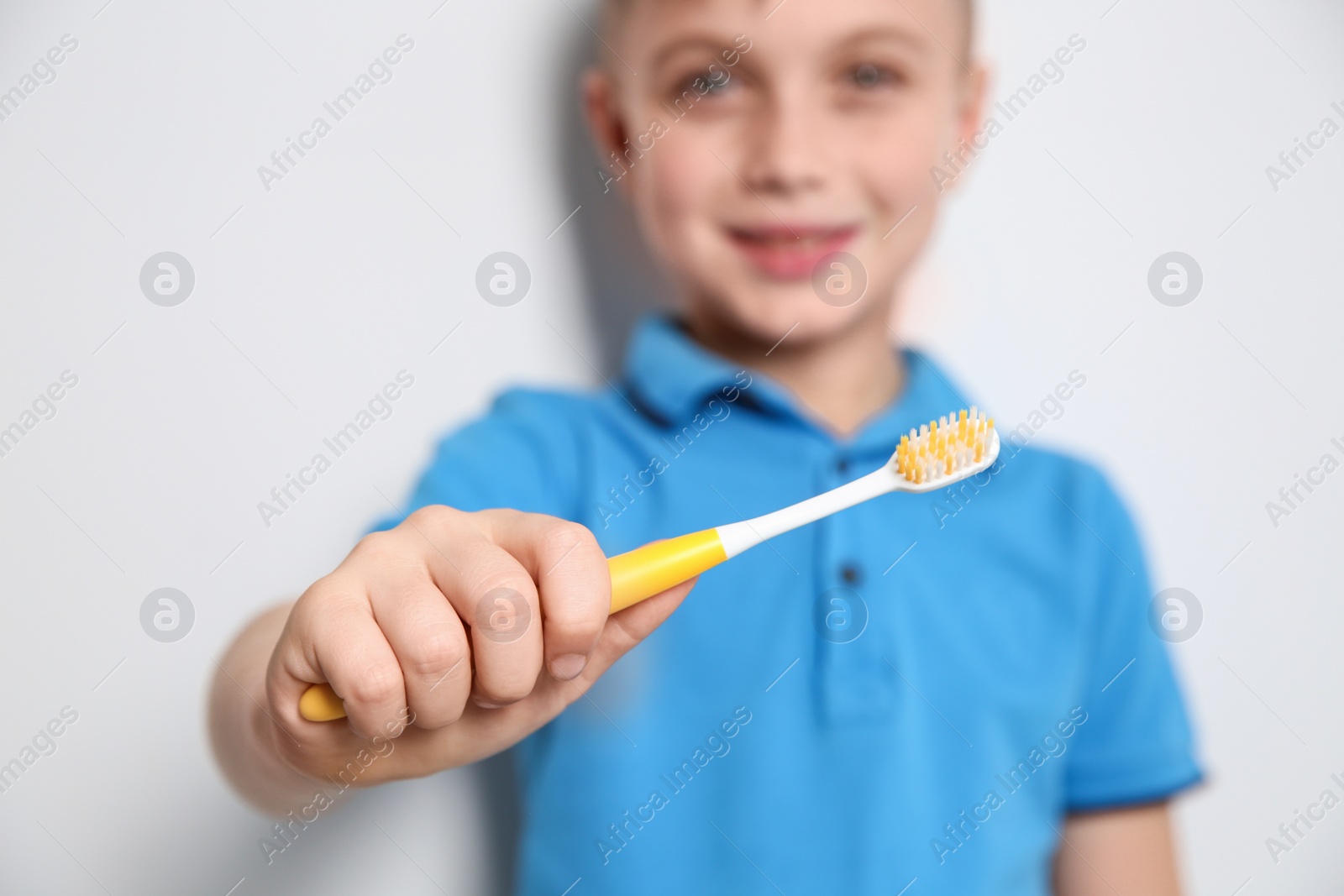 Photo of Little boy with toothbrush on light background, focus on hand