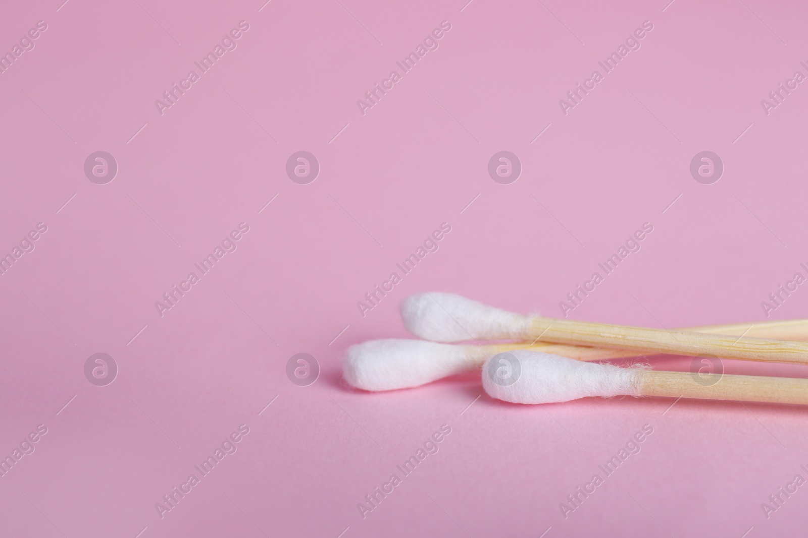 Photo of Wooden cotton buds on pink background, closeup. Space for text