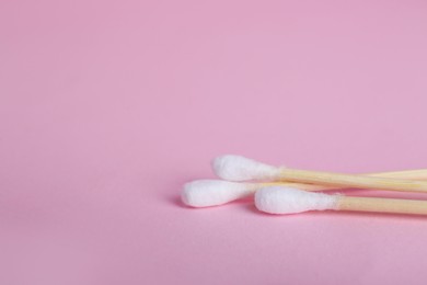 Photo of Wooden cotton buds on pink background, closeup. Space for text