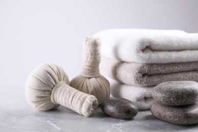 Fresh towels, spa stones and herbal bags on grey table, space for text