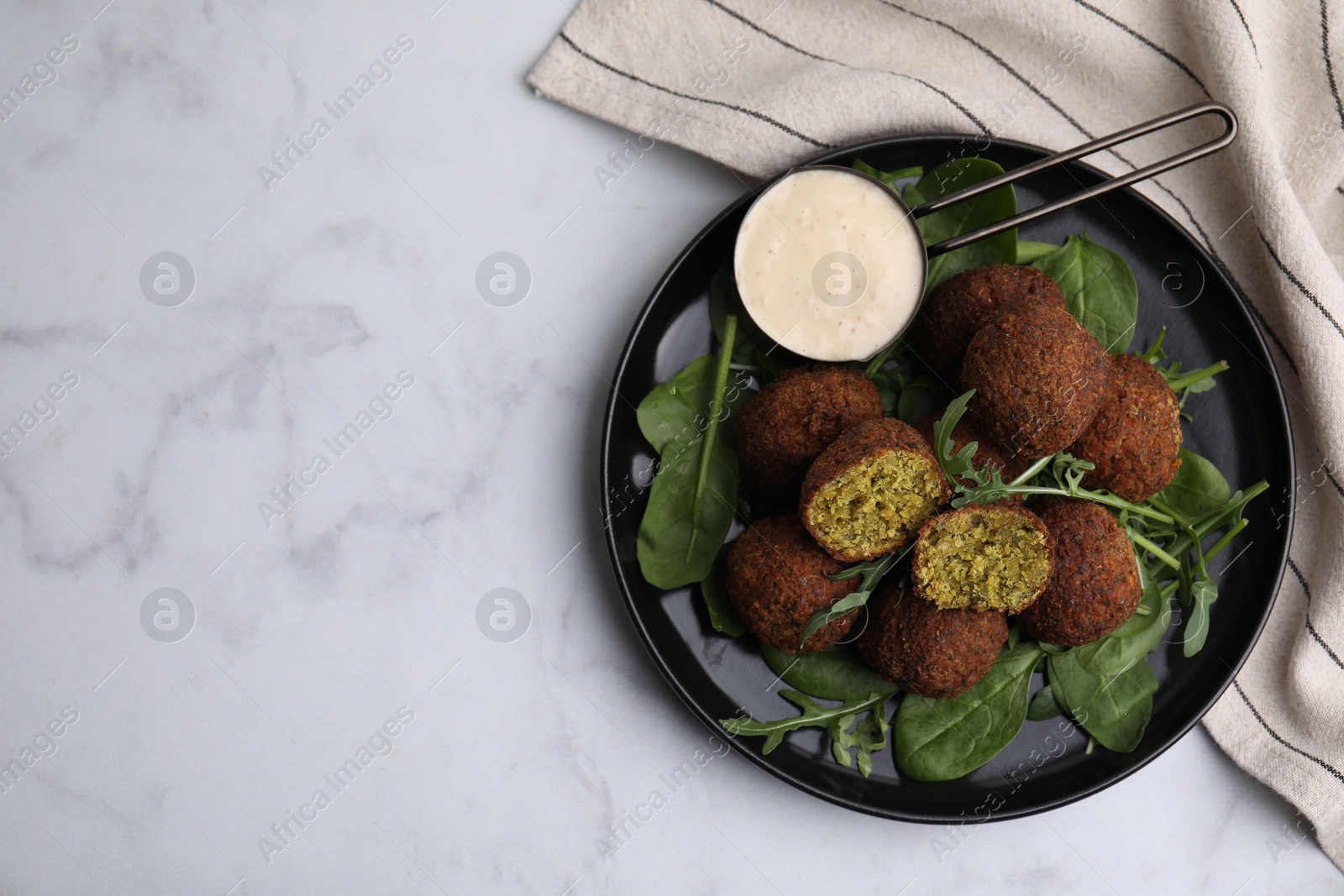 Photo of Delicious falafel balls, herbs and sauce on white marble table, top view. Space for text