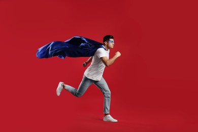 Photo of Man in superhero cape and mask running on red background
