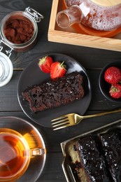 Tasty chocolate sponge cake served on black wooden table, flat lay