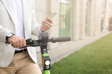 Photo of Businessman with modern kick scooter using smartphone on city street, closeup. Space for text