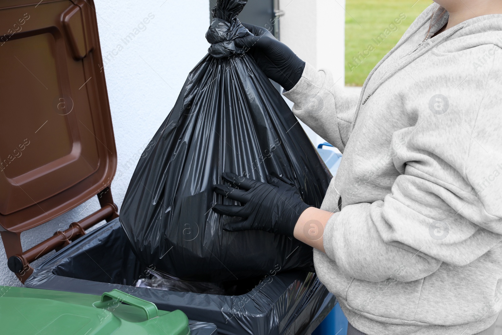 Photo of Woman throwing trash bag full of garbage in bin outdoors, closeup. Recycling concept