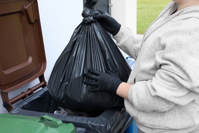 Photo of Woman throwing trash bag full of garbage in bin outdoors, closeup. Recycling concept