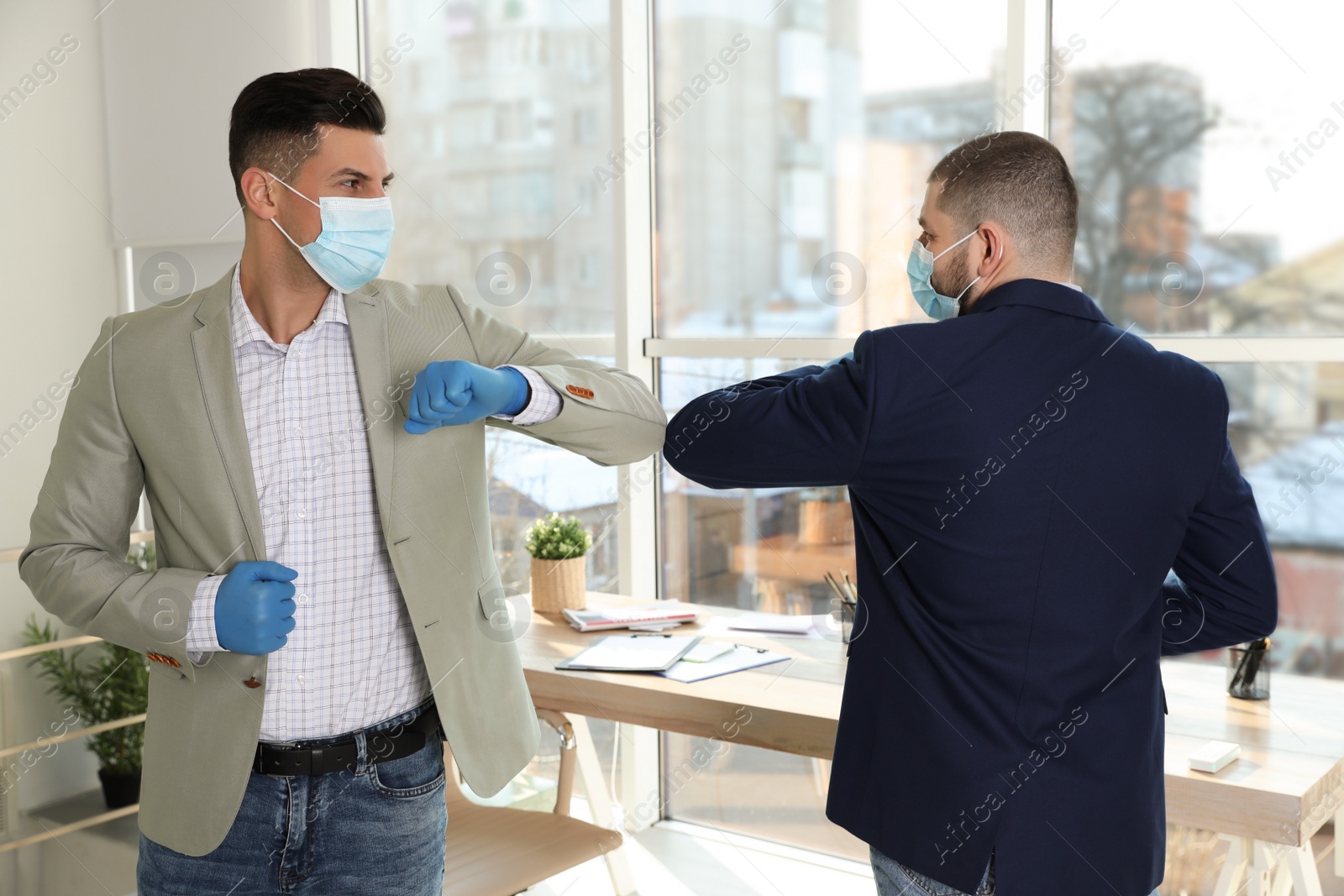 Photo of Office employees in masks greeting each other by bumping elbows at workplace