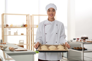 Photo of Female pastry chef holding baking sheet with uncooked croissants in kitchen