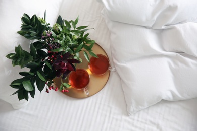 Photo of Tray with cups of tea and floral decor near soft blanket on bed