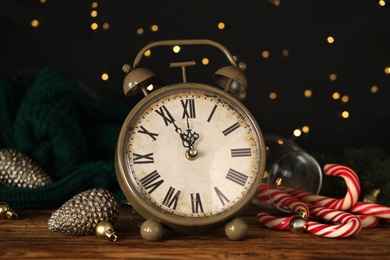 Vintage alarm clock and decor on wooden table against blurred Christmas lights, closeup. New Year countdown