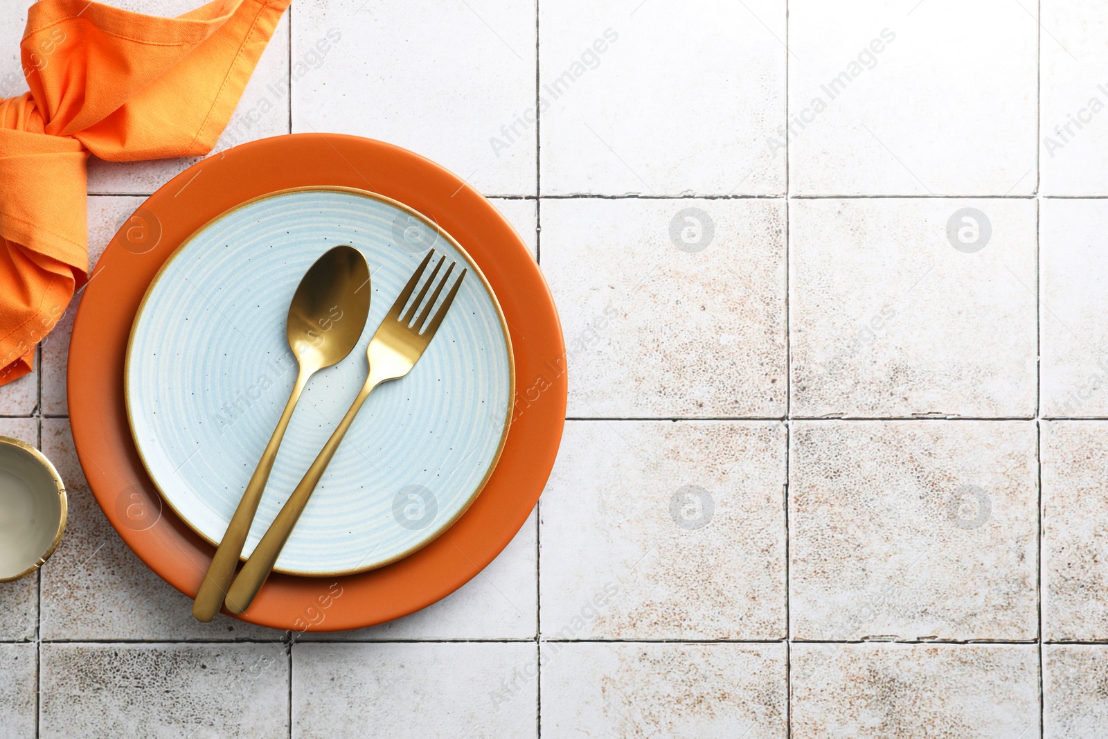 Photo of Stylish setting with cutlery, napkin and plates on light tiled table, top view. Space for text