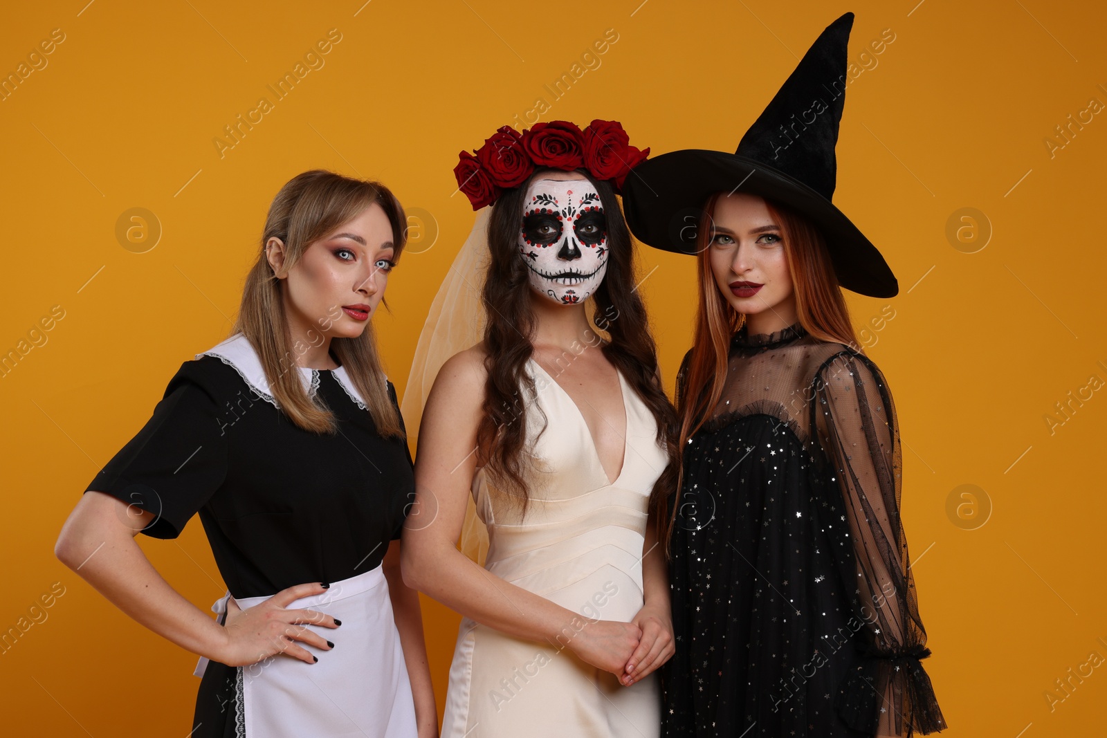 Photo of Women in scary costumes on orange background. Halloween celebration