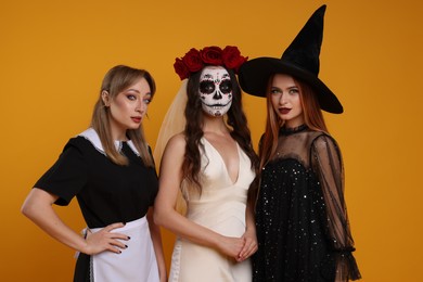 Women in scary costumes on orange background. Halloween celebration