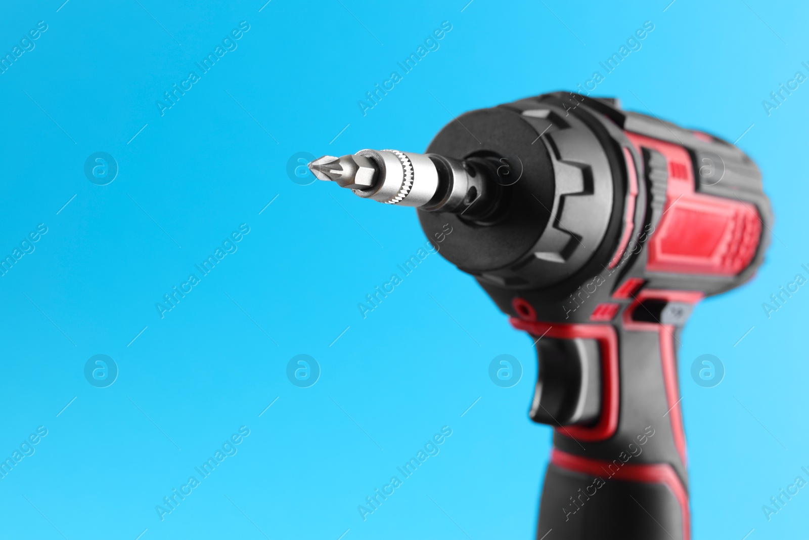 Photo of Modern electric screwdriver on light blue background, closeup. Space for text