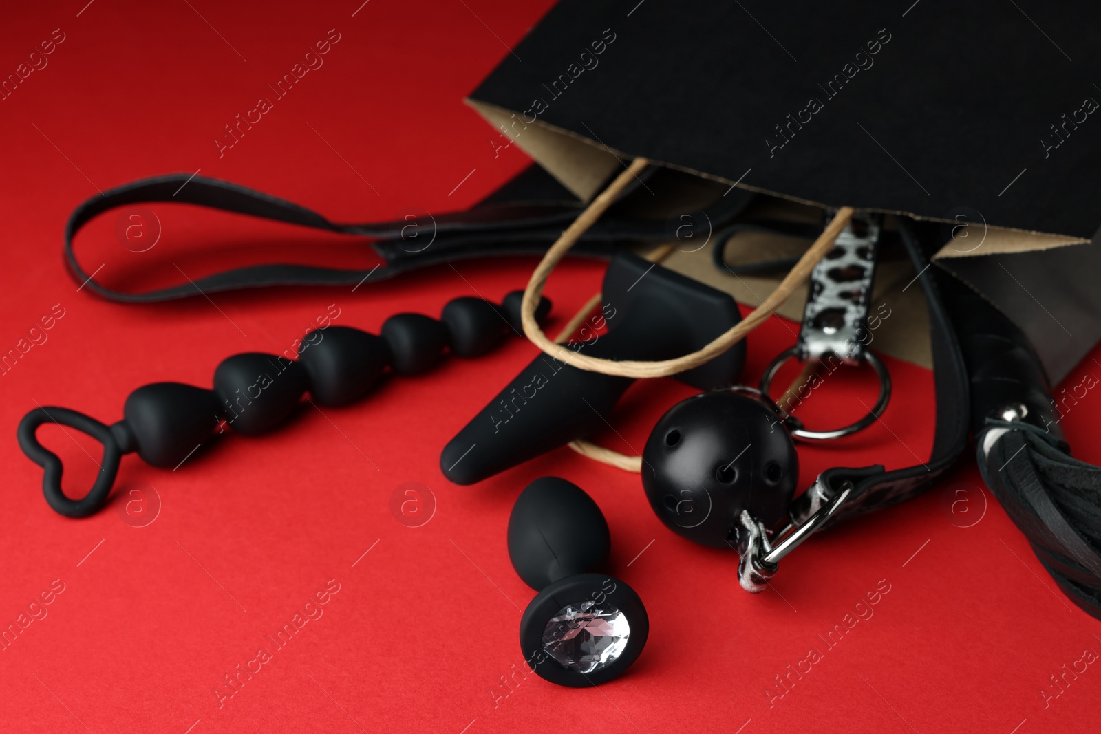 Photo of Shopping bag and different sex toys on red background