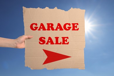 Woman holding sign with text GARAGE SALE against blue sky