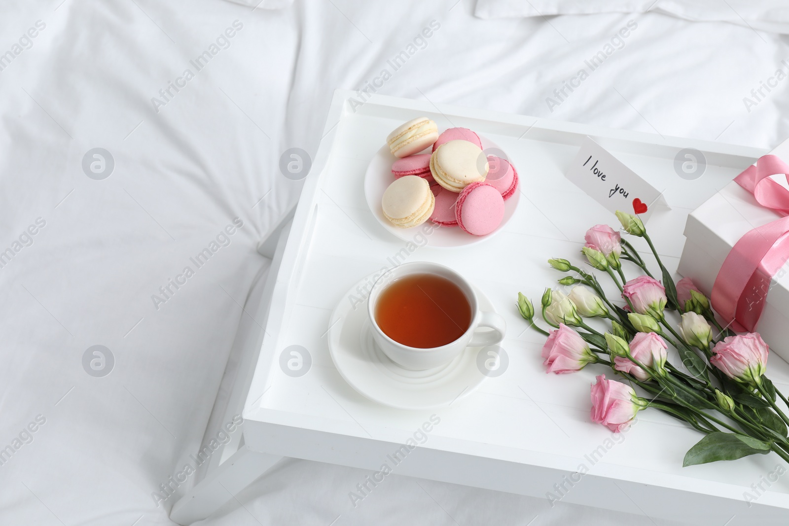 Photo of Tasty breakfast served in bed. Delicious macarons, tea, gift box, flowers and I Love You card on tray, space for text