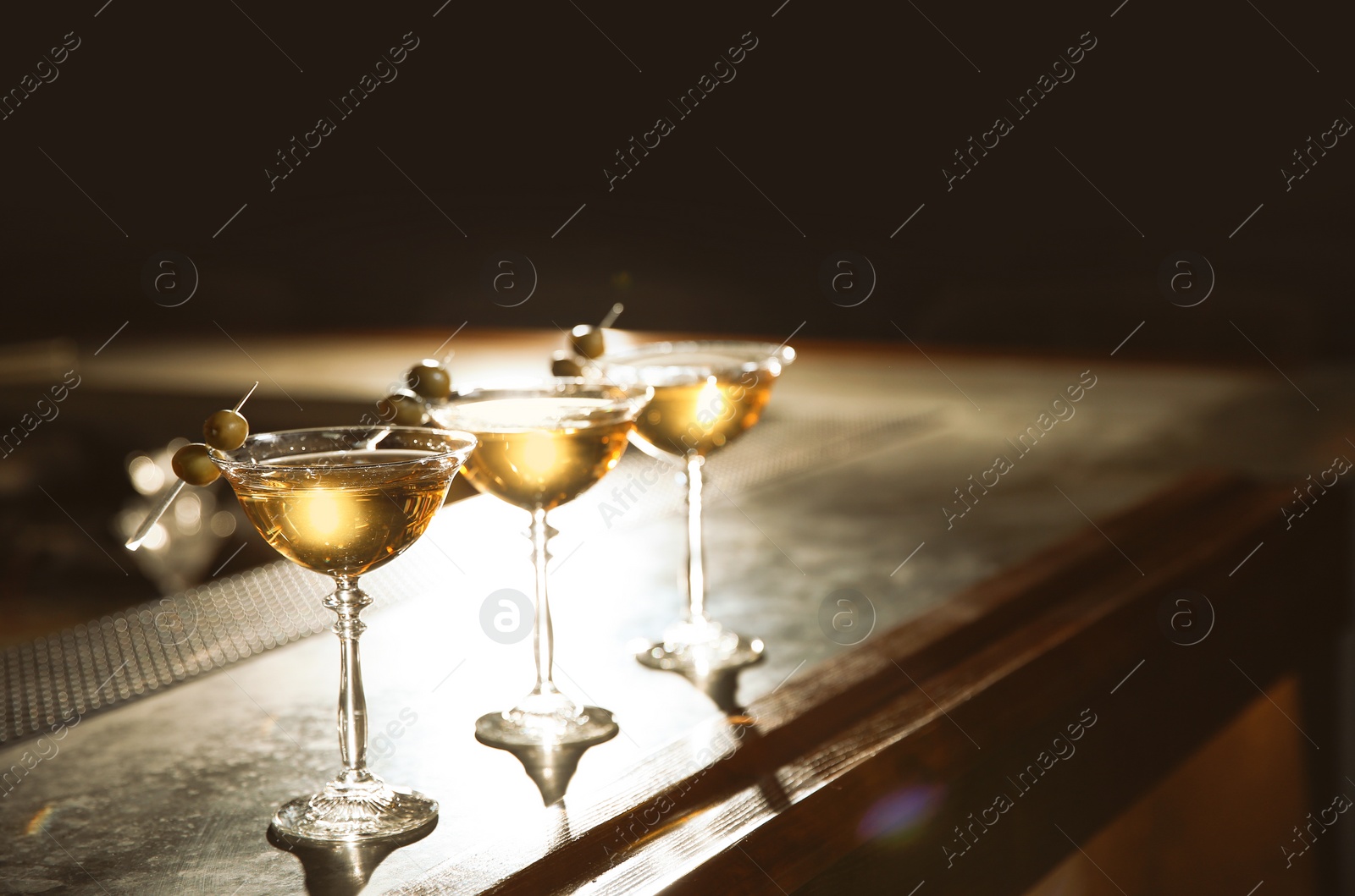 Photo of Glasses of martini cocktail with olives on bar counter. Space for text