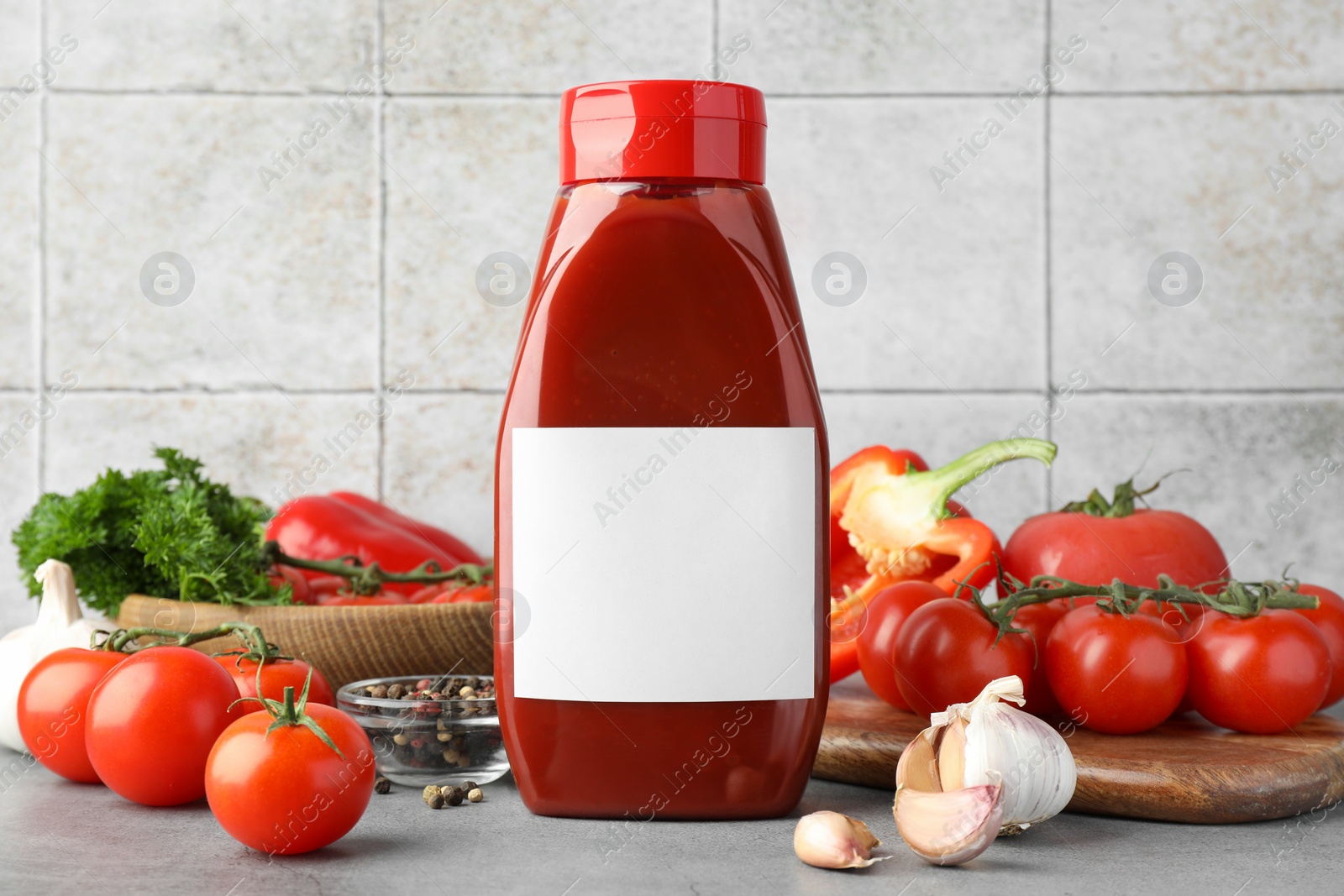 Photo of Bottle of tasty ketchup and ingredients on grey table. Space for text