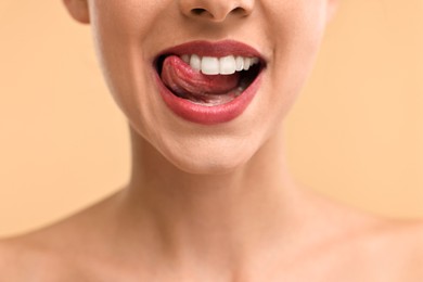 Photo of Woman with beautiful lips licking her teeth on beige background, closeup
