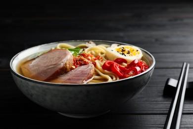 Photo of Delicious ramen in bowl and chopsticks on black wooden table, closeup. Noodle soup