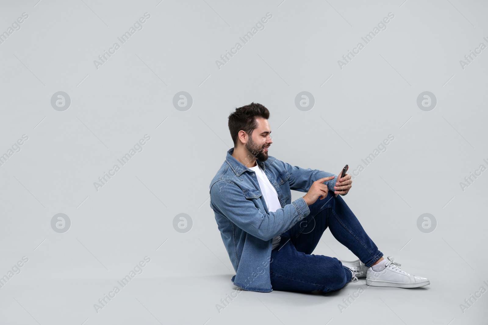 Photo of Handsome young man using smartphone on grey background, space for text