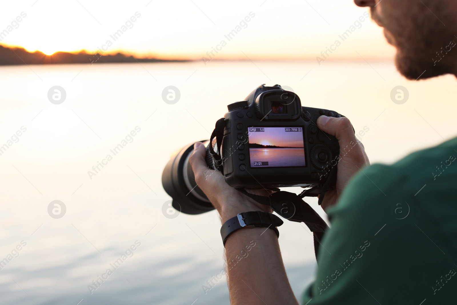 Photo of Male photographer holding professional camera with photo of riverside sunset on display