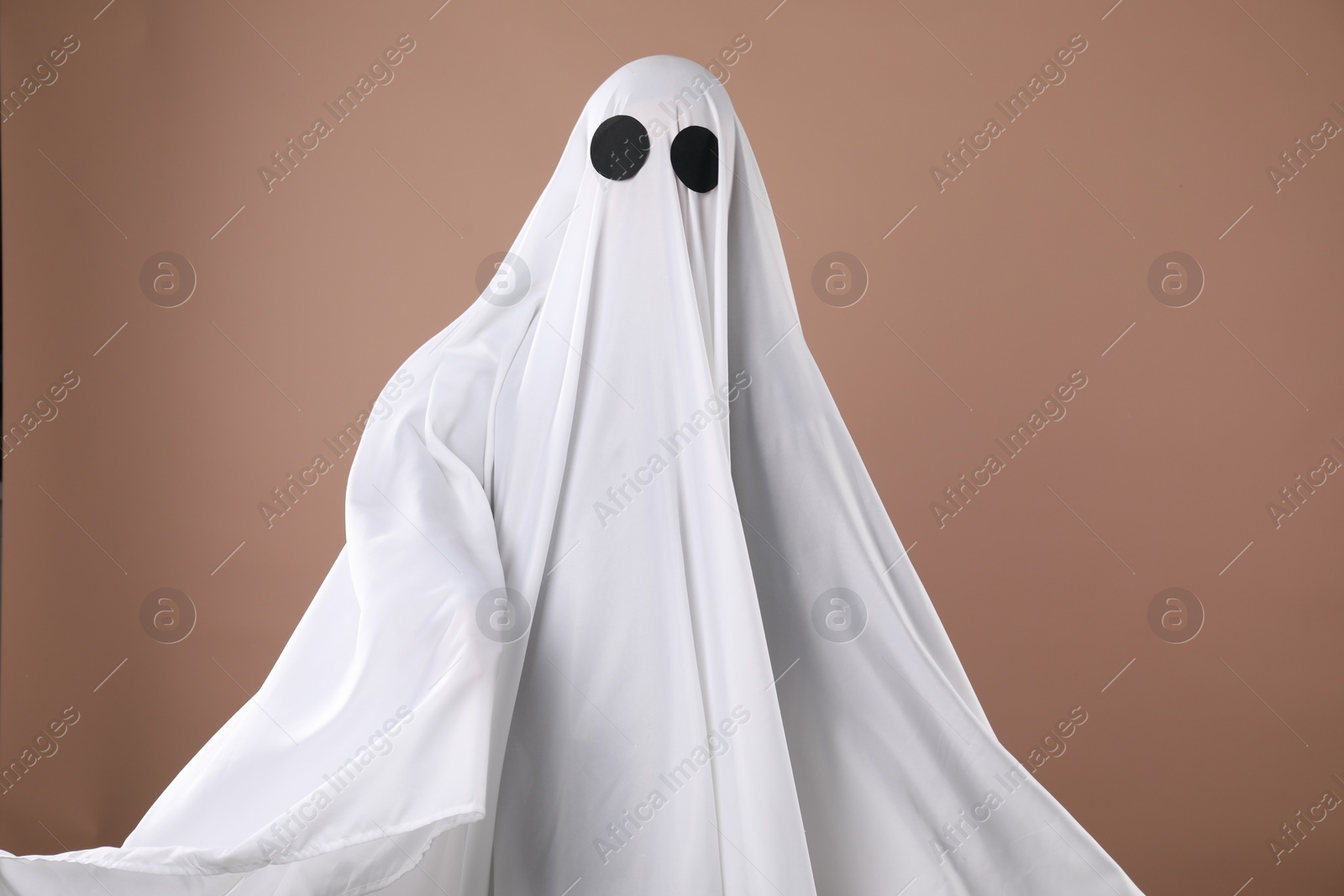 Photo of Creepy ghost. Person covered with white sheet on dark beige background