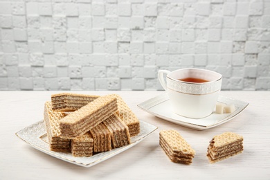 Photo of Plate of delicious wafers with cup of tea on white wooden table