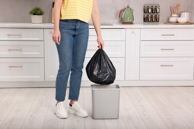 Photo of Woman taking garbage bag out of trash bin in kitchen, closeup