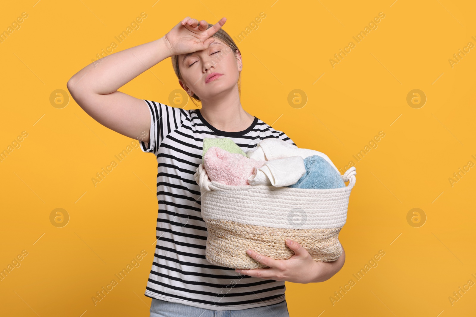 Photo of Tired woman with basket full of laundry on orange background