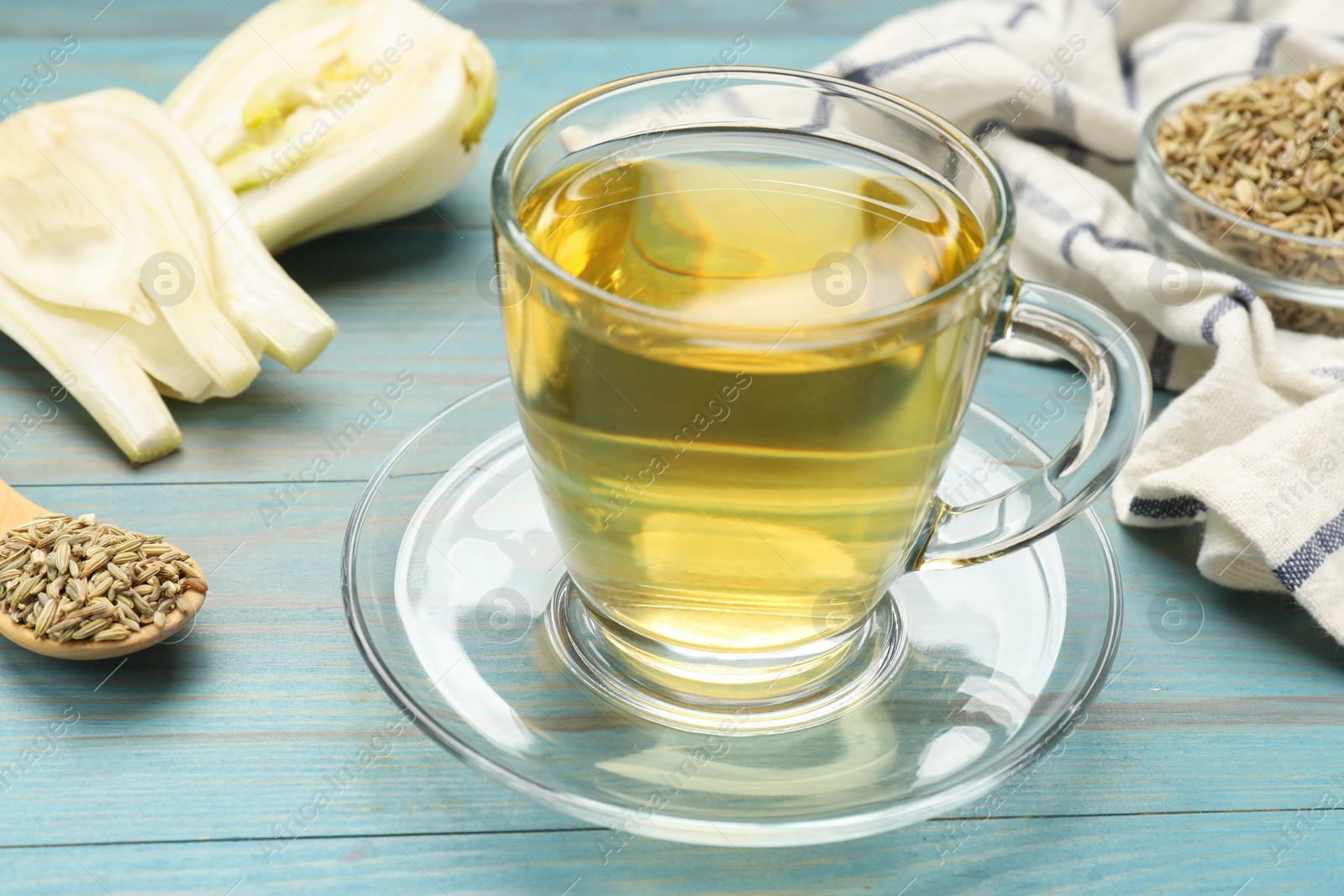 Photo of Aromatic fennel tea, seeds and fresh vegetable on light blue wooden table, closeup