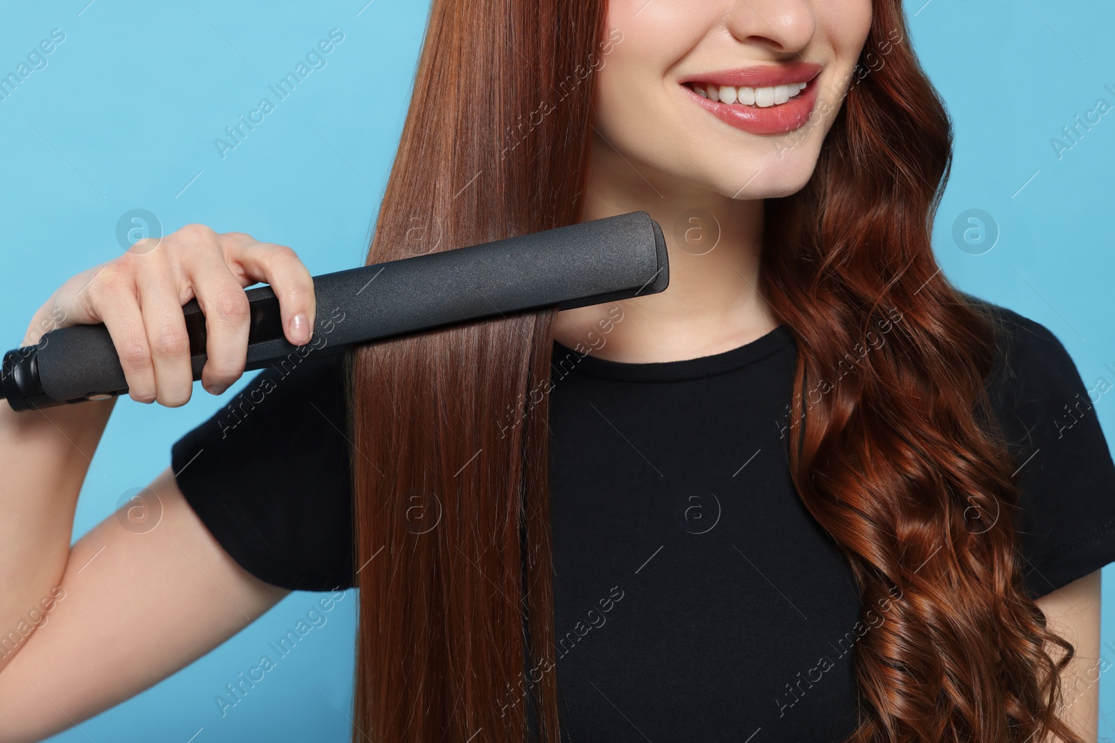 Photo of Young woman using hair iron on light blue background, closeup