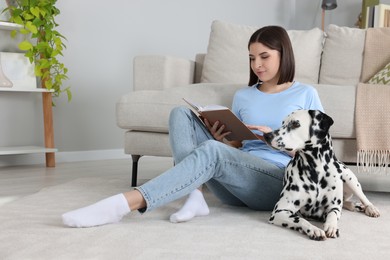 Photo of Beautiful young woman reading book and her adorable Dalmatian dog on floor at home. Lovely pet