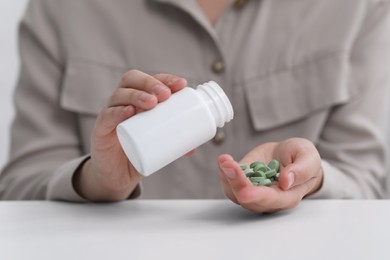 Photo of Woman pouring antidepressants from bottle at white table, closeup