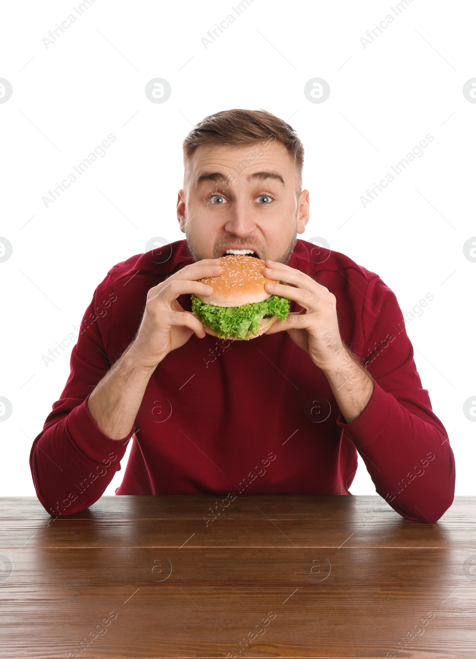 Photo of Young man eating tasty burger at table on white background