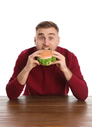 Young man eating tasty burger at table on white background