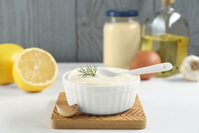 Photo of Fresh mayonnaise sauce in bowl and ingredients on white table