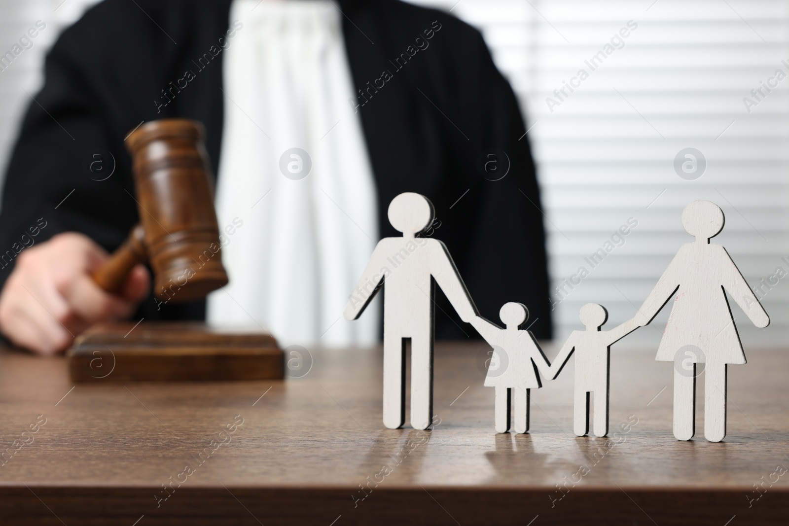 Photo of Family law. Judge with gavel sitting at wooden table, focus on figure of parents and children