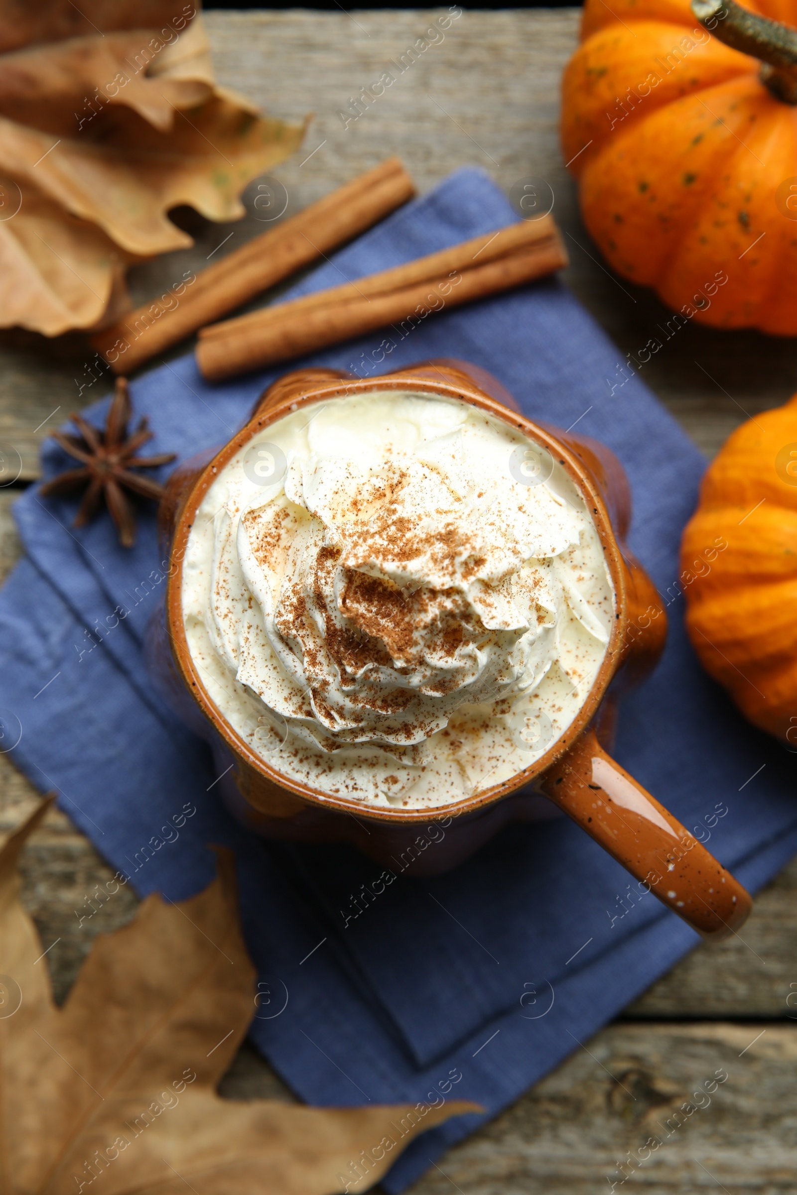 Photo of Mug of pumpkin spice latte with whipped cream, ingredients and dry leaves on wooden table, flat lay