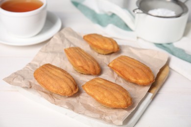 Photo of Tasty madeleine cookies and cup of tea on white wooden table