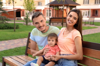 Photo of Happy family with adorable little baby on bench outdoors