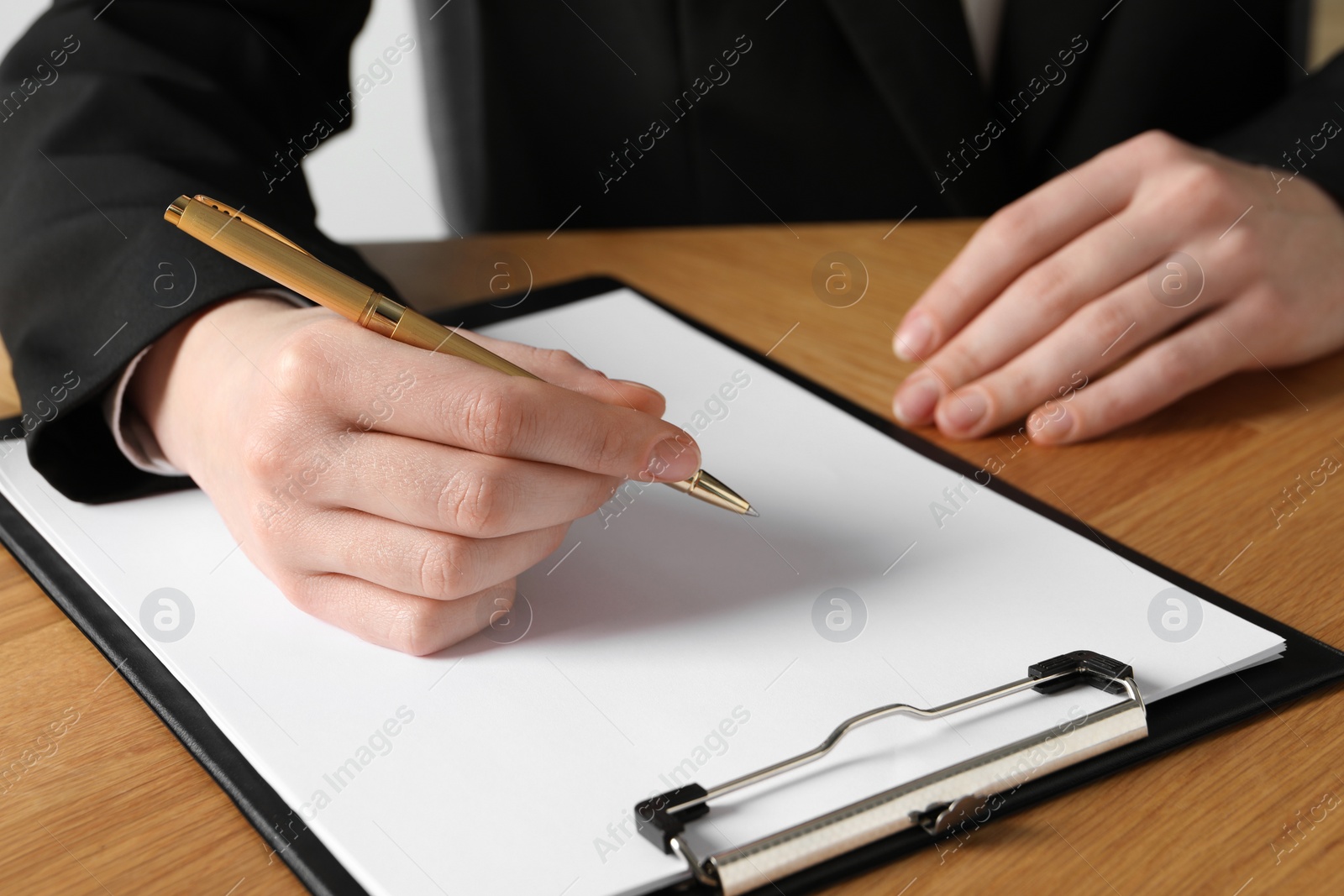 Photo of Woman with pen and clipboard at wooden table, closeup