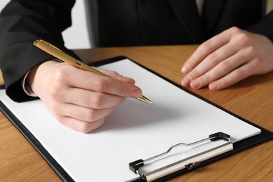 Woman with pen and clipboard at wooden table, closeup