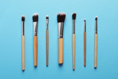 Photo of Different makeup brushes on light blue background, flat lay