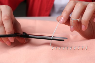 Photo of Woman cutting sewing thread over cloth, closeup