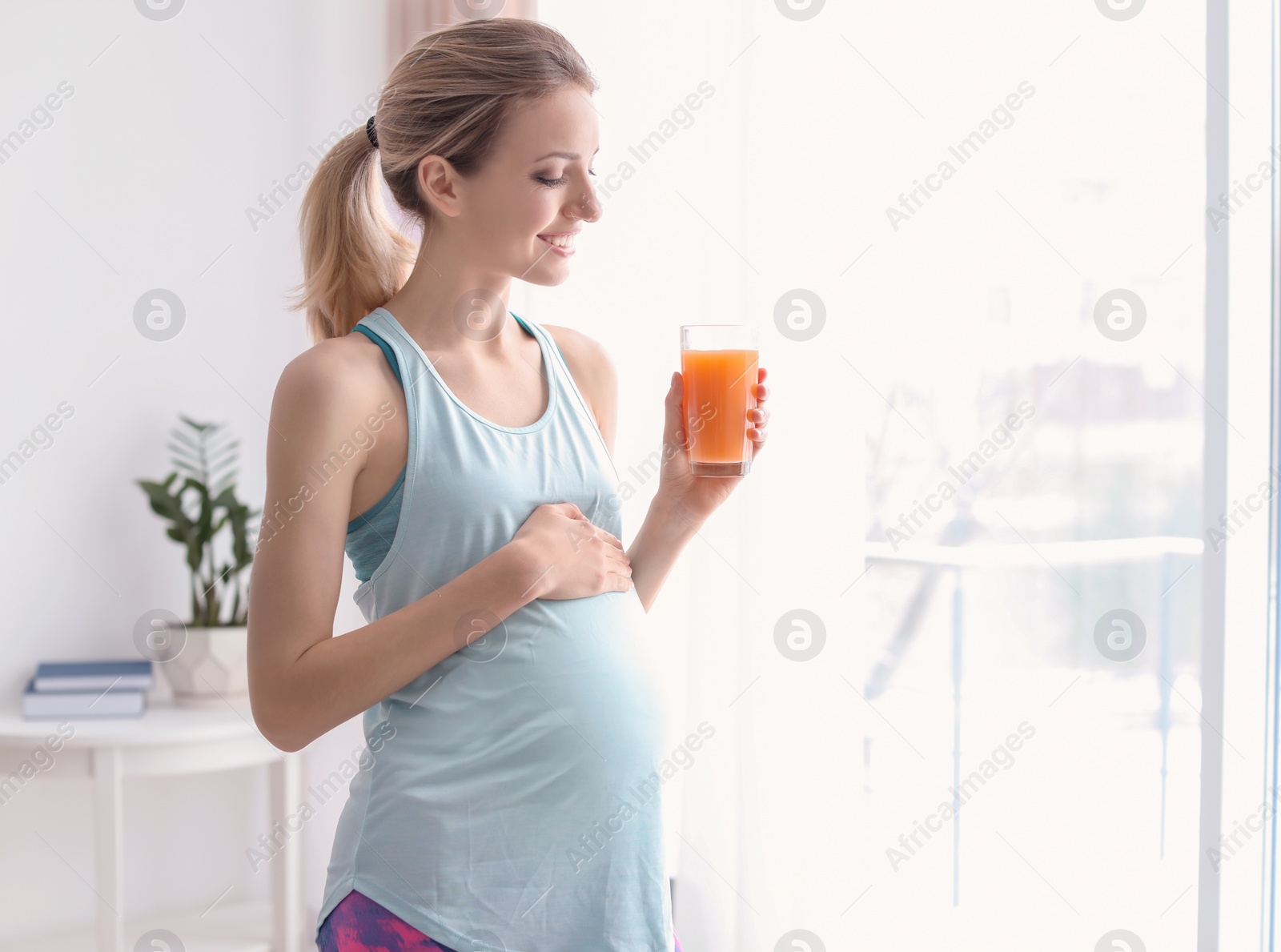 Photo of Young pregnant woman holding glass with juice at home