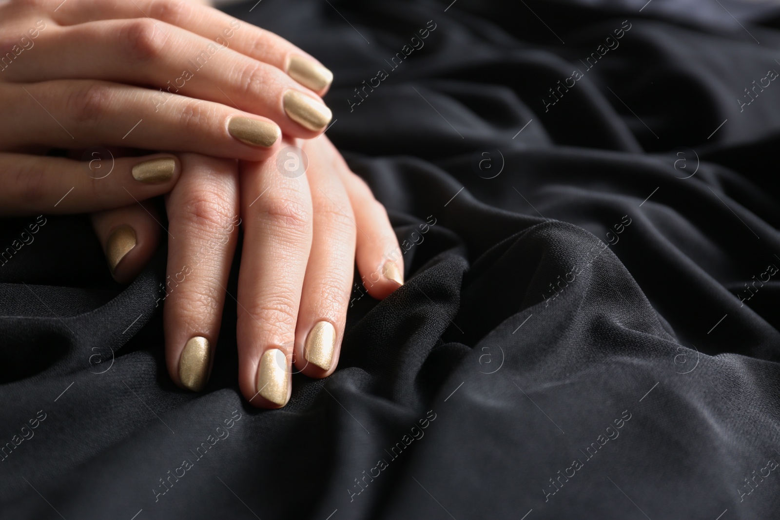 Photo of Woman showing gold manicure on black fabric, closeup with space for text. Nail polish trends