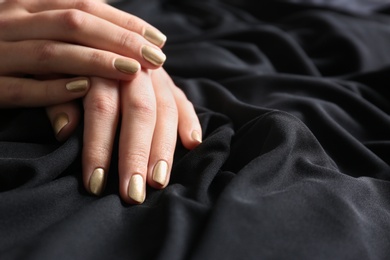 Photo of Woman showing gold manicure on black fabric, closeup with space for text. Nail polish trends