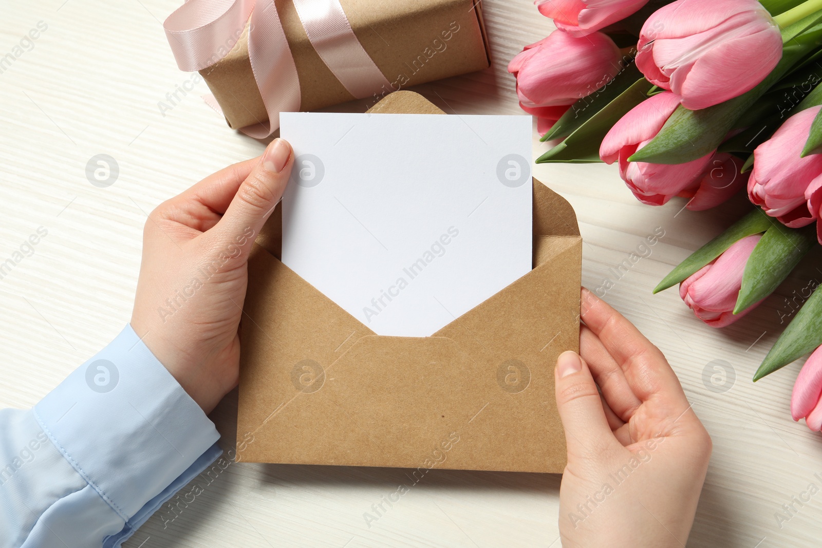 Photo of Happy Mother's Day. Woman holding envelope with blank card at white wooden table, top view